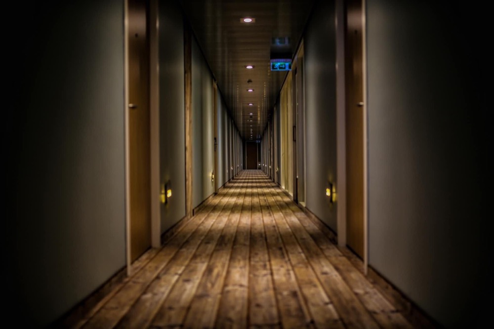 Langer, dunkler Hotelflur mit Holzboden und Türen auf beiden Seiten, die in die Ferne führen.